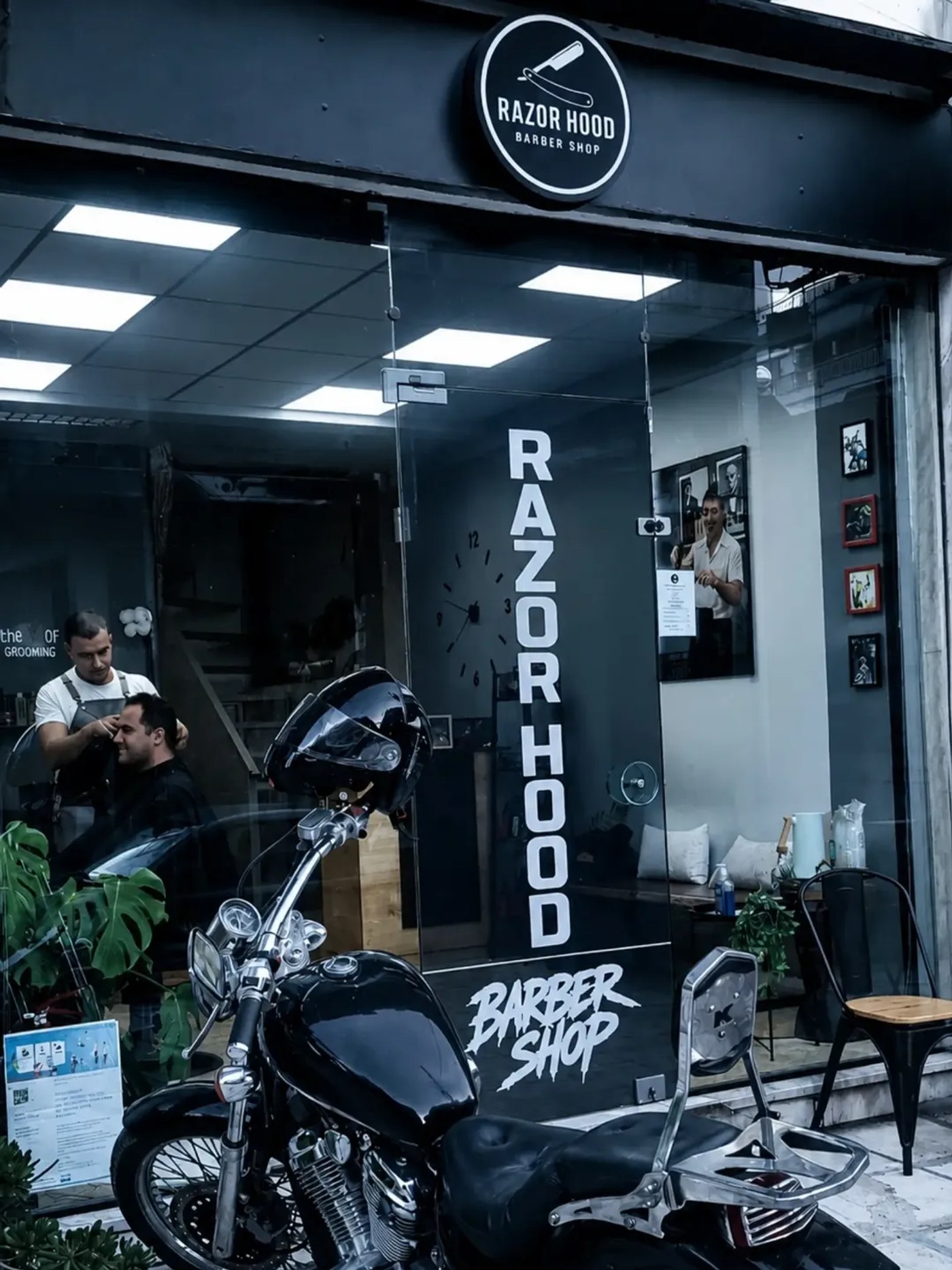 Η βιτρίνα του Razor Hood Barber Shop, με μηχανή σταθμευμένη μέσα στο μαγαζί και τον barber να δουλεύει
